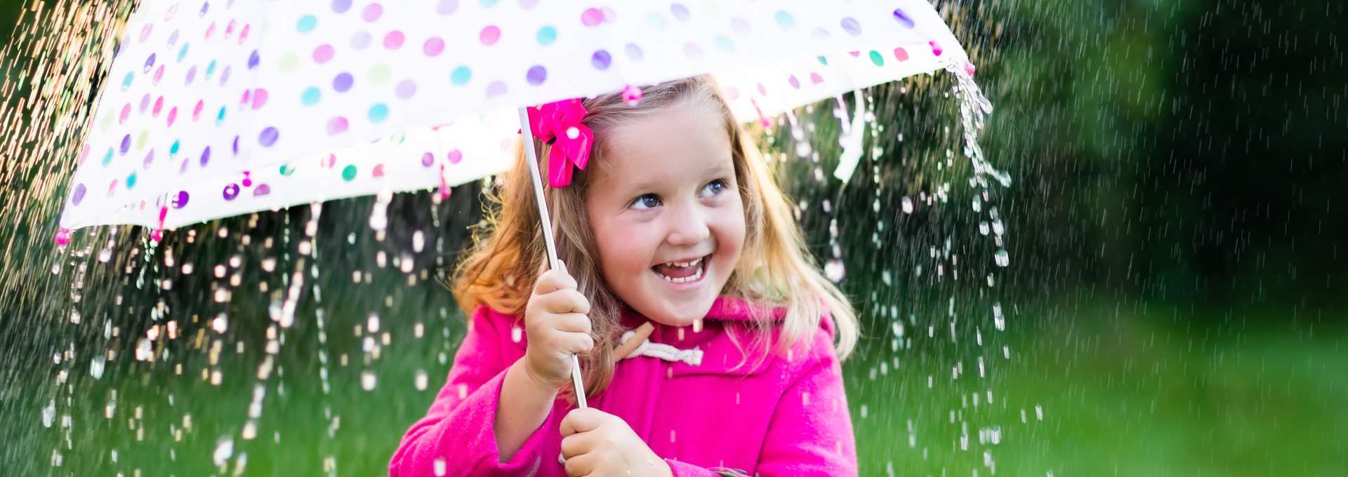 en flicka i rosa jacka som står med ett paraply i regnet